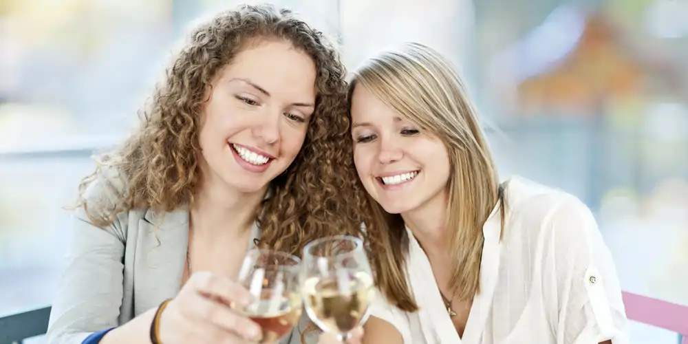 two smiling girlfriends each enjoying a glass of wine at wineries on a winery tour