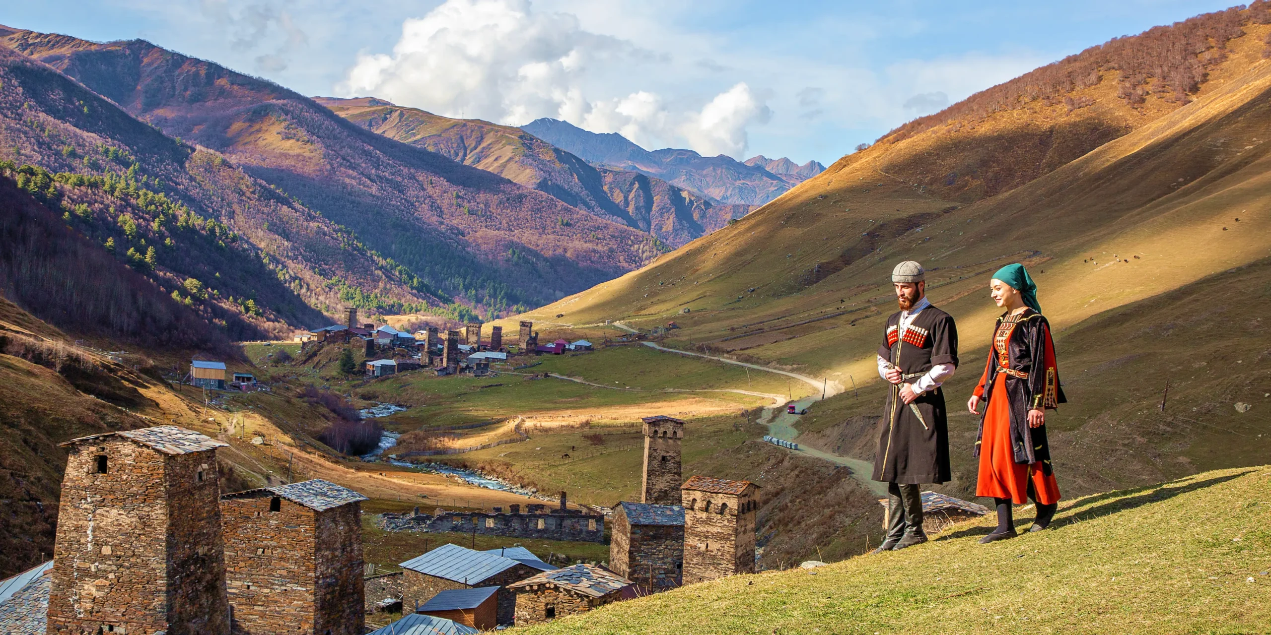 traditional-clothed-georgian-couple-in-caucasus-mountains-ushguli-georgia A traditionally clothed Georgian couple walks down a hillside towards a village in the Caucasus Mountains, a region deeply connected to the origin of wine