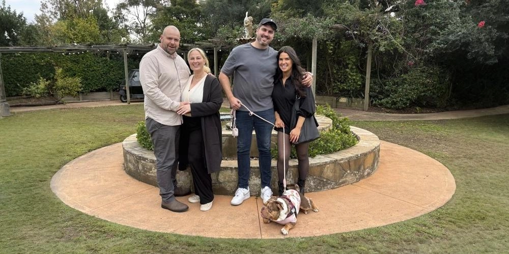 Young couple with their British bulldog enjoying a Hunter Valley dog friendly wine tour alongside her mother and her mother’s fiancé, surrounded by vineyard views and wine glasses in hand